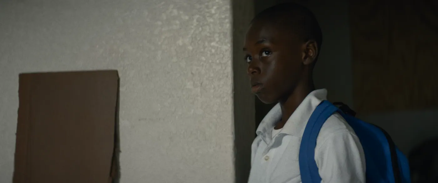 Moonlight (2016), Barry Jenkins — plan rapproché, intérieur, un personnage, clair-obscur : polo blanc, sac à dos bleu, sac à dos, carton