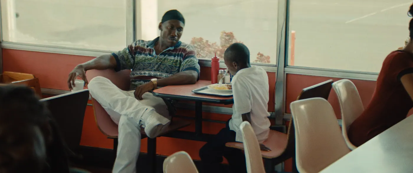 Moonlight (2016), Barry Jenkins — plan large, jour, intérieur, quatre personnages, lumière de fenêtre : restaurant, pantalon blanc, polo blanc, plateau, assiette, bouteille de ketchup