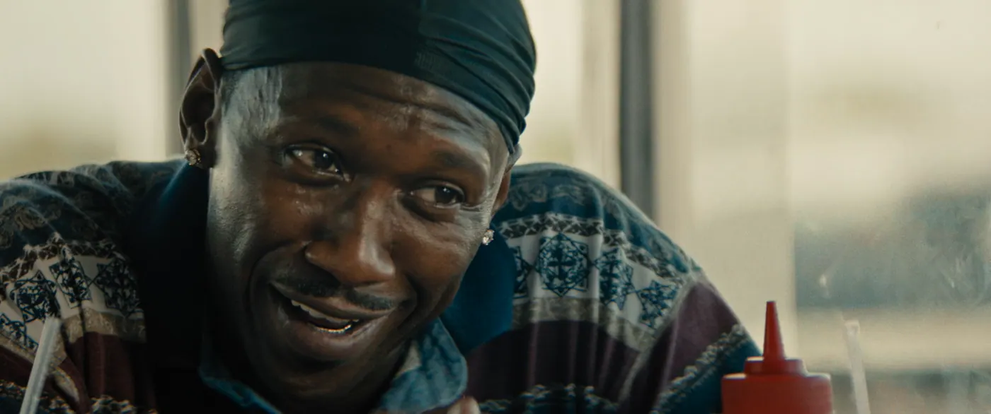 Moonlight (2016), Barry Jenkins — gros plan, jour, intérieur, un personnage : restaurant, bouteille de ketchup, paille, boucle d’oreille, durag, polo, rire