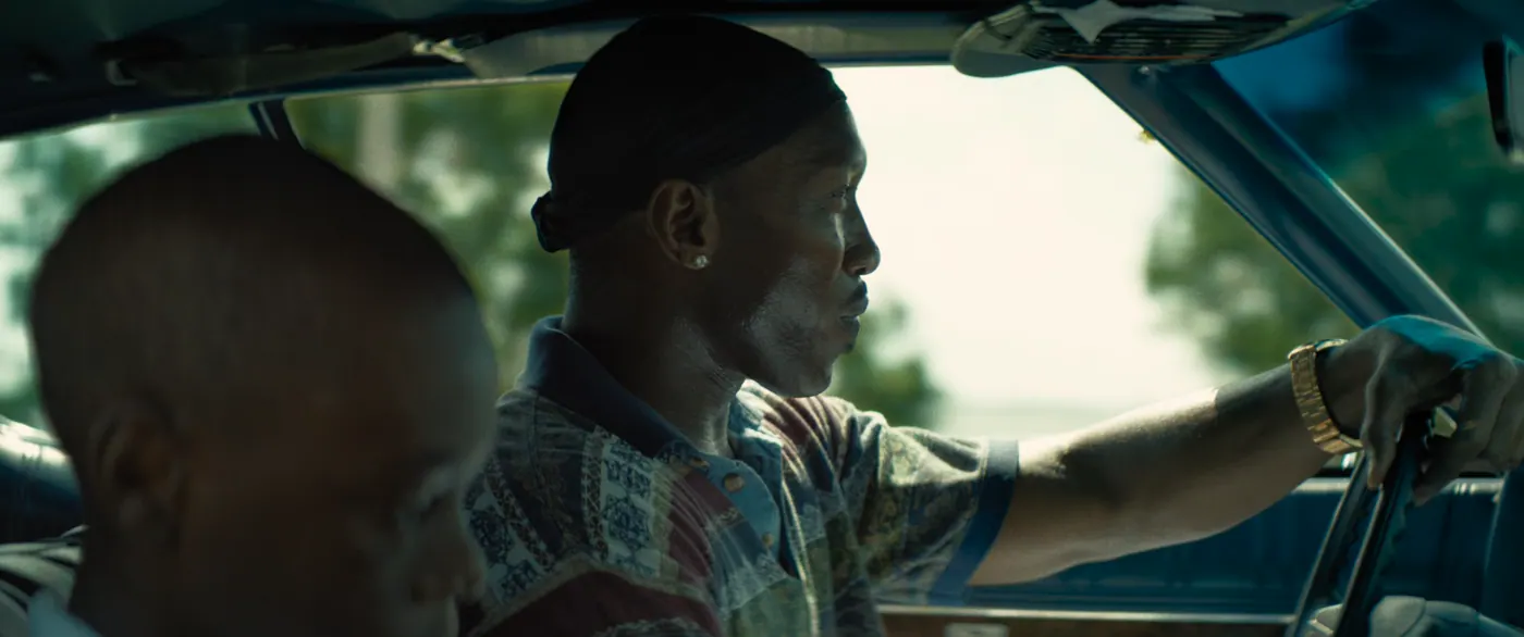 Moonlight (2016), Barry Jenkins — plan rapproché, jour, intérieur, deux personnages : voiture (habitacle), voiture, volant, montre, boucle d’oreille, durag, polo, conduire