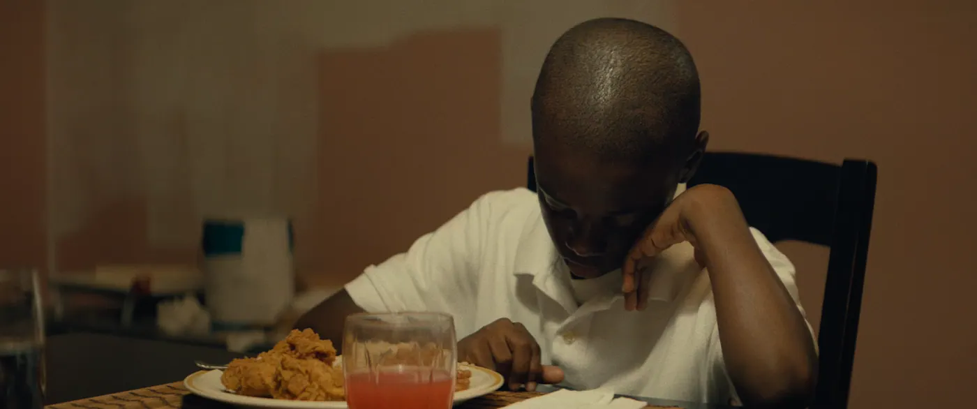 Moonlight (2016), Barry Jenkins — plan rapproché, intérieur, un personnage, lumière chaude : cuisine, polo blanc, poulet frit, assiette, verre, fourchette, serviette