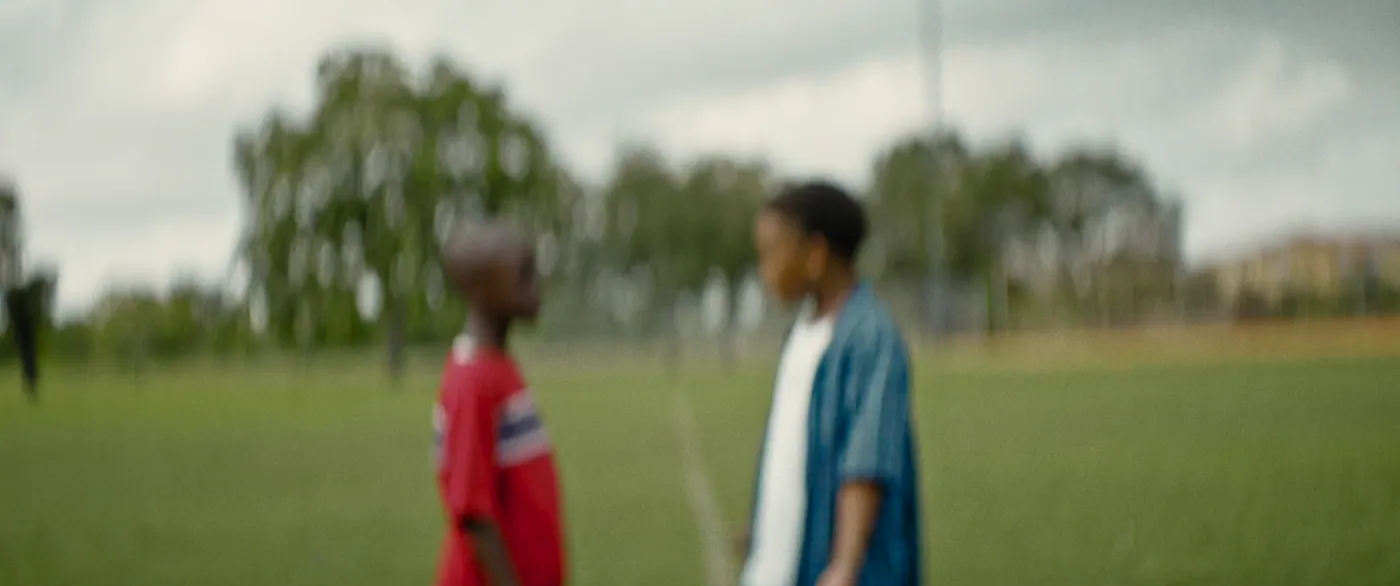 Moonlight (2016), Barry Jenkins — plan moyen, jour, extérieur, deux personnages : terrain de sport, tee-shirt rouge, chemise bleue