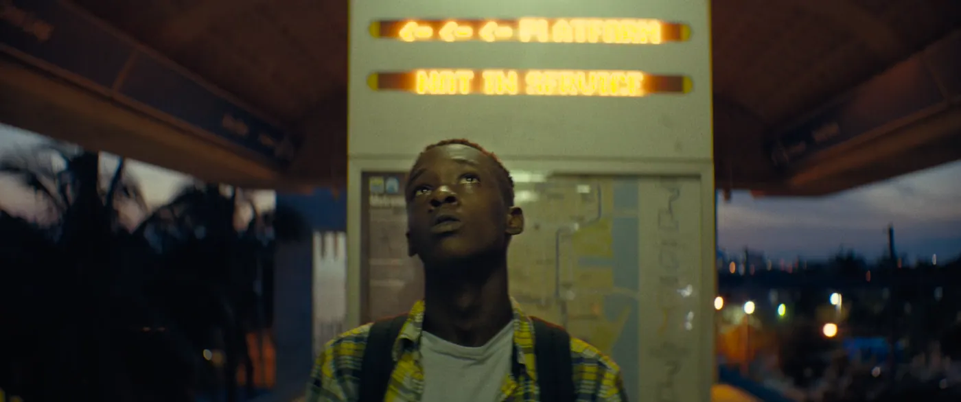 Moonlight (2016), Barry Jenkins — plan rapproché, aube ou crépuscule, extérieur, un personnage, lumière chaude : métro, panneau lumineux, plan du métro, sac à dos, palmier
