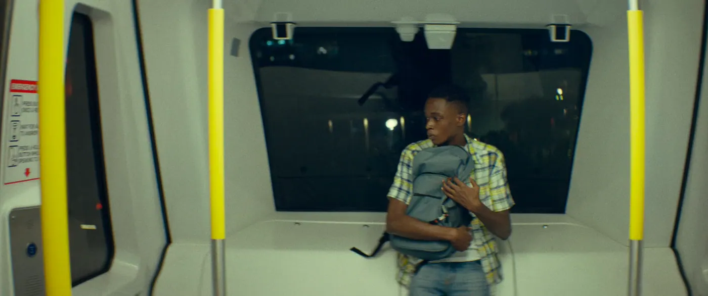 Moonlight (2016), Barry Jenkins — plan moyen, nuit, intérieur, un personnage, lumière froide : métro, sac à dos, barre de maintien, fenêtre, chemise à carreaux, jean, voyager