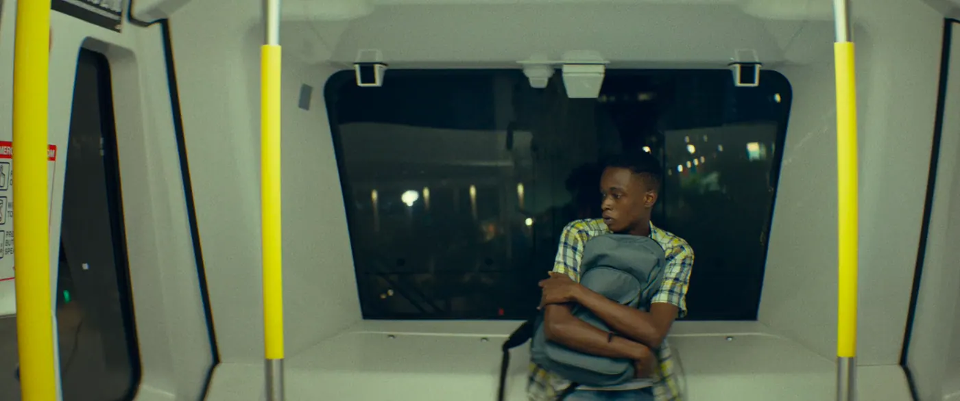 Moonlight (2016), Barry Jenkins — plan moyen, nuit, intérieur, un personnage, lumière froide : métro, sac à dos, barre de maintien, fenêtre, chemise à carreaux, jean, voyager