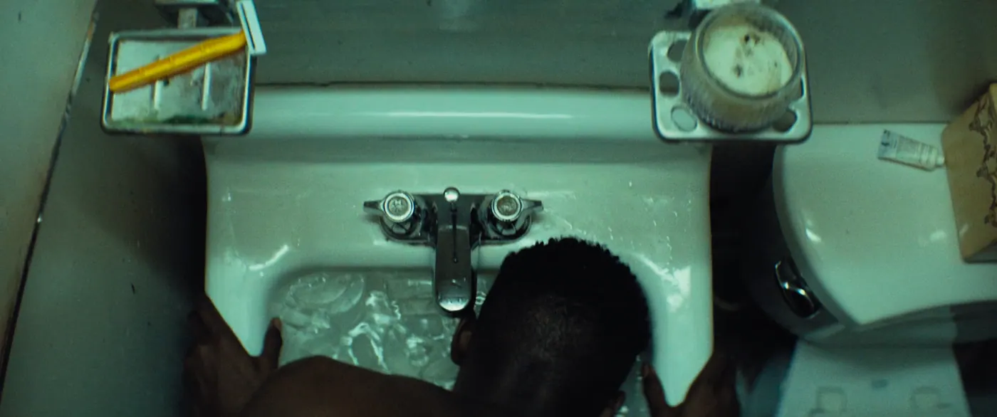Moonlight (2016), Barry Jenkins — plan rapproché, intérieur, un personnage, lumière froide : salle de bain, lavabo, robinet, glaçon, porte-savon, toilettes, torse nu