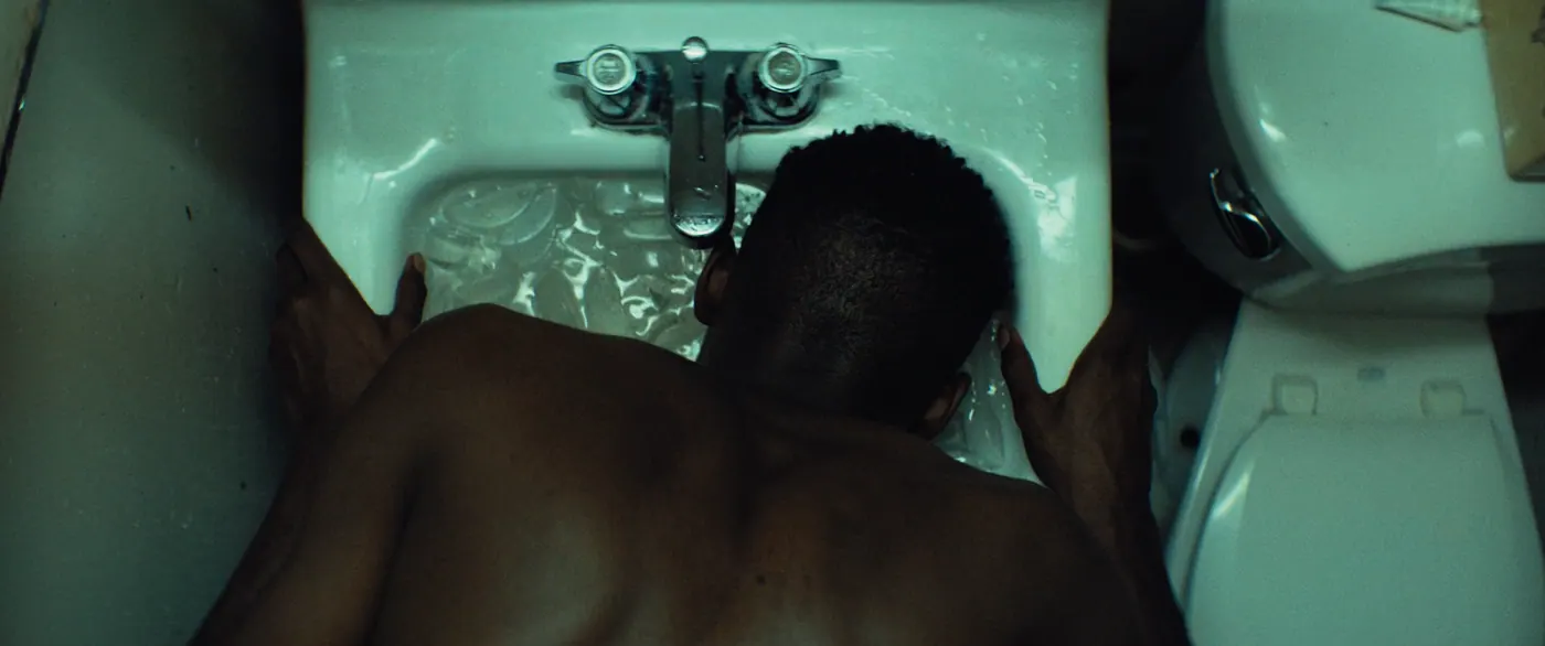 Moonlight (2016), Barry Jenkins — plan rapproché, intérieur, un personnage, lumière froide : salle de bain, lavabo, robinet, glaçon, toilettes, torse nu
