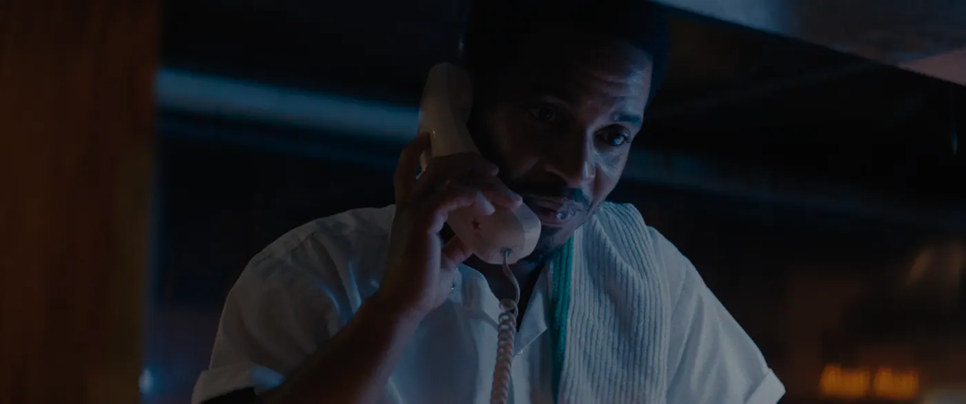 Moonlight (2016), Barry Jenkins — plan rapproché, nuit, intérieur, un personnage, lumière froide : restaurant, chemise blanche, téléphone fixe, serviette, téléphoner