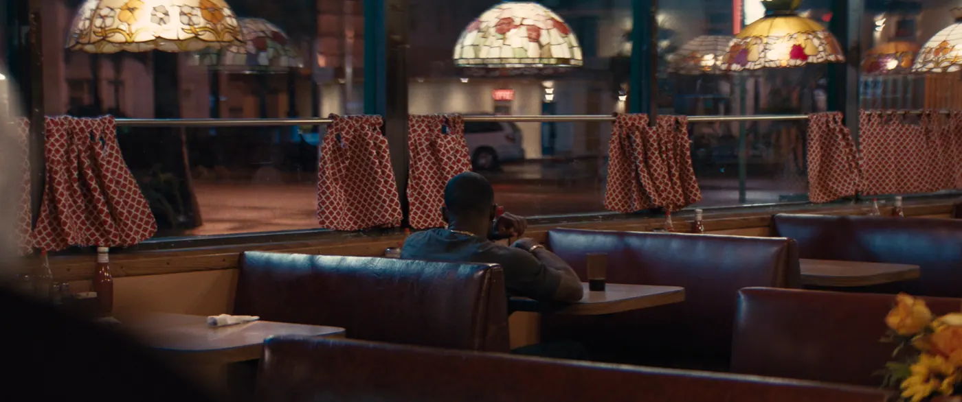Moonlight (2016), Barry Jenkins — plan large, nuit, intérieur, un personnage, lumière chaude : restaurant, lampe tiffany, rideau, banquette, table, fenêtre, tee-shirt, attendre