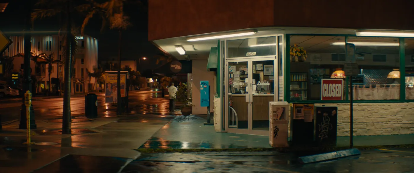 Moonlight (2016), Barry Jenkins — plan d’ensemble, nuit, extérieur, un personnage, néon, lumière froide : restaurant, rue, enseigne, pancarte, néon, palmier, parcmètre, marcher