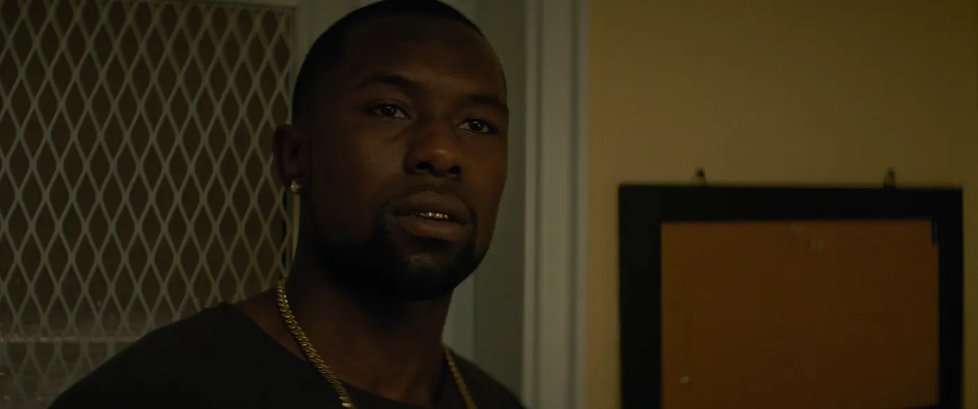 Moonlight (2016), Barry Jenkins — gros plan, nuit, intérieur, un personnage, lumière chaude : dent en or, chaîne en or, boucle d’oreille, grille, tableau de liège, tee-shirt