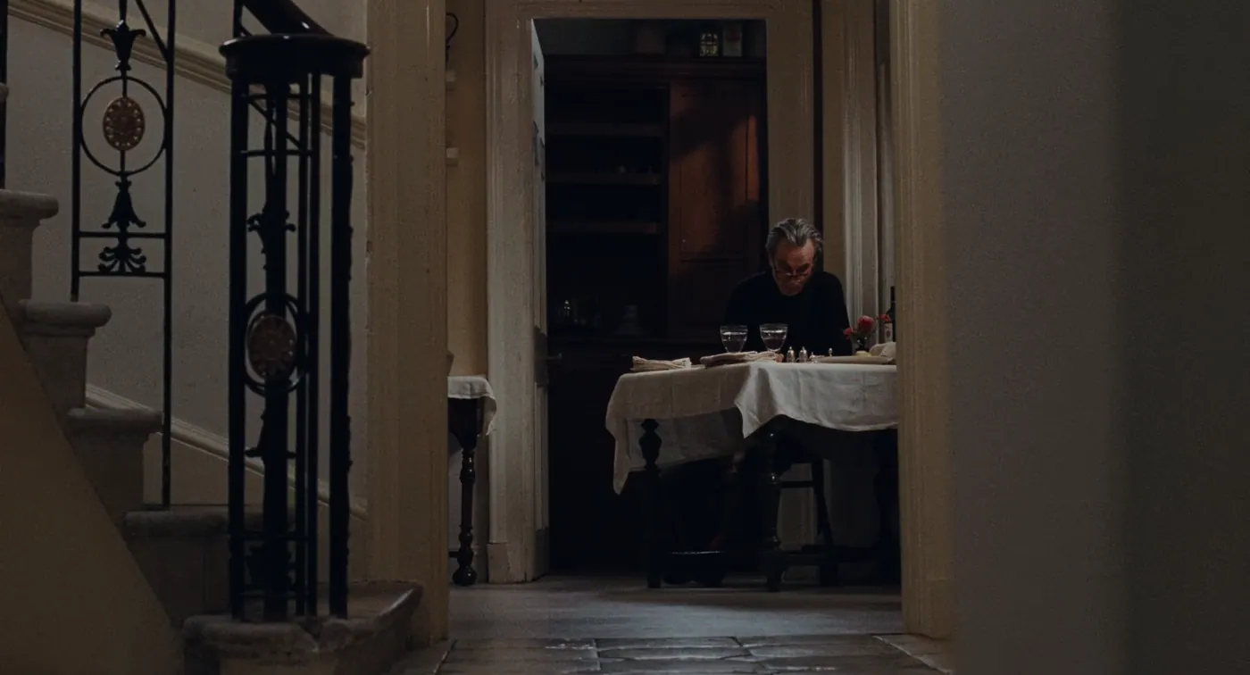 Phantom Thread (2017), Paul Thomas Anderson — plan large, intérieur, un personnage, lumière chaude : escalier, couloir, pull noir, table, nappe, verre, salière, bouquet de fleurs, lunettes