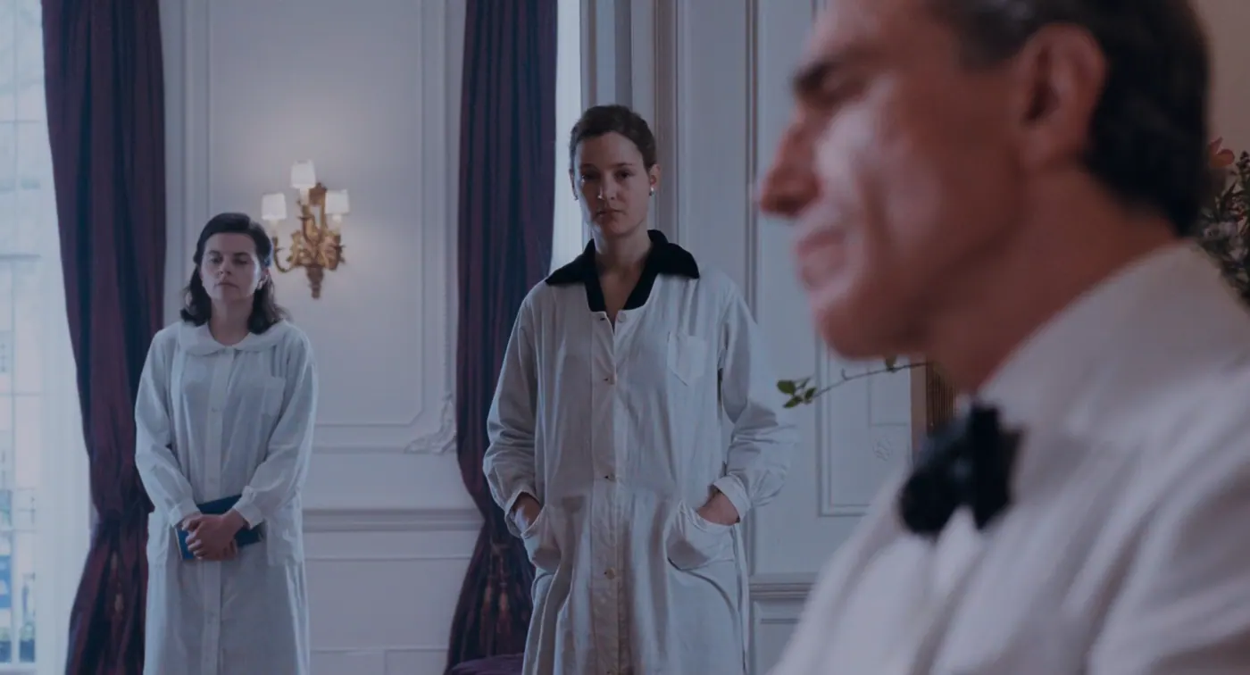 Phantom Thread (2017), Paul Thomas Anderson — plan rapproché, jour, intérieur, trois personnages, lumière de fenêtre : salon, blouse blanche, nœud papillon noir, applique, rideau, fenêtre