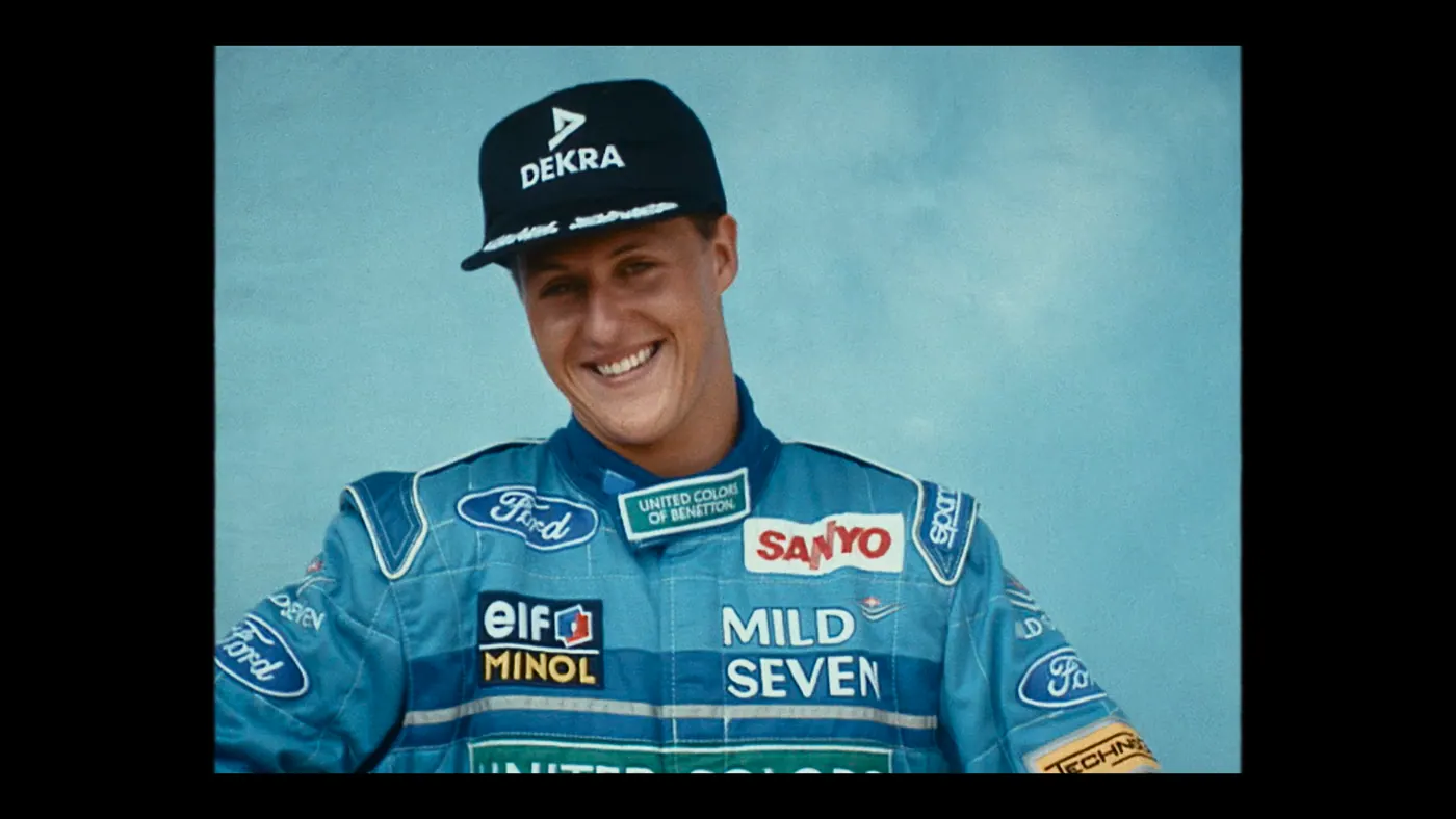 Schumacher ’94 — The Birth of a Legend (2026), Christin Freitag — plan rapproché, un personnage : casquette noire, combinaison bleue, combinaison de pilote, rire