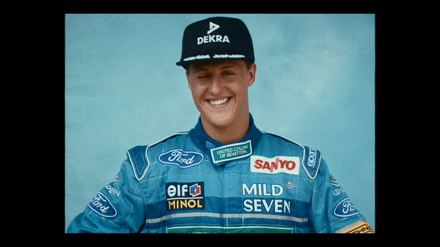 Schumacher ’94 — The Birth of a Legend (2026), Christin Freitag — plan rapproché, un personnage : casquette noire, combinaison bleue, combinaison de pilote, rire