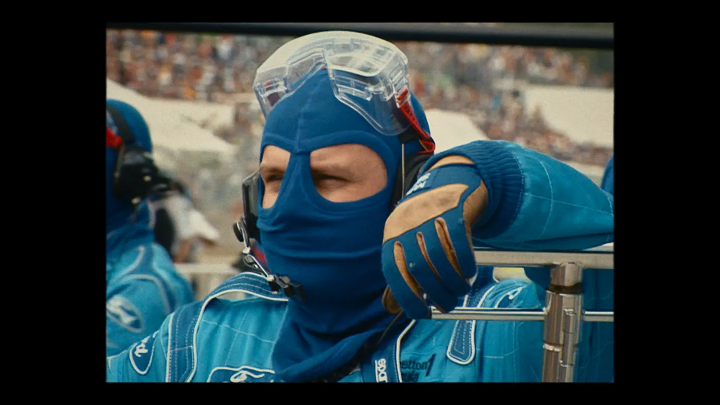 Schumacher ’94 — The Birth of a Legend (2026), Christin Freitag — plan rapproché, jour, extérieur, foule : circuit automobile, voie des stands, cagoule bleue, combinaison bleue
