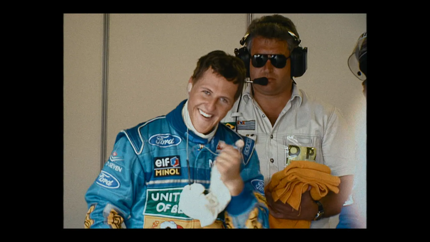 Schumacher ’94 — The Birth of a Legend (2026), Christin Freitag — plan rapproché, intérieur, trois personnages : garage, combinaison bleue, serviette, combinaison de pilote, casque audio