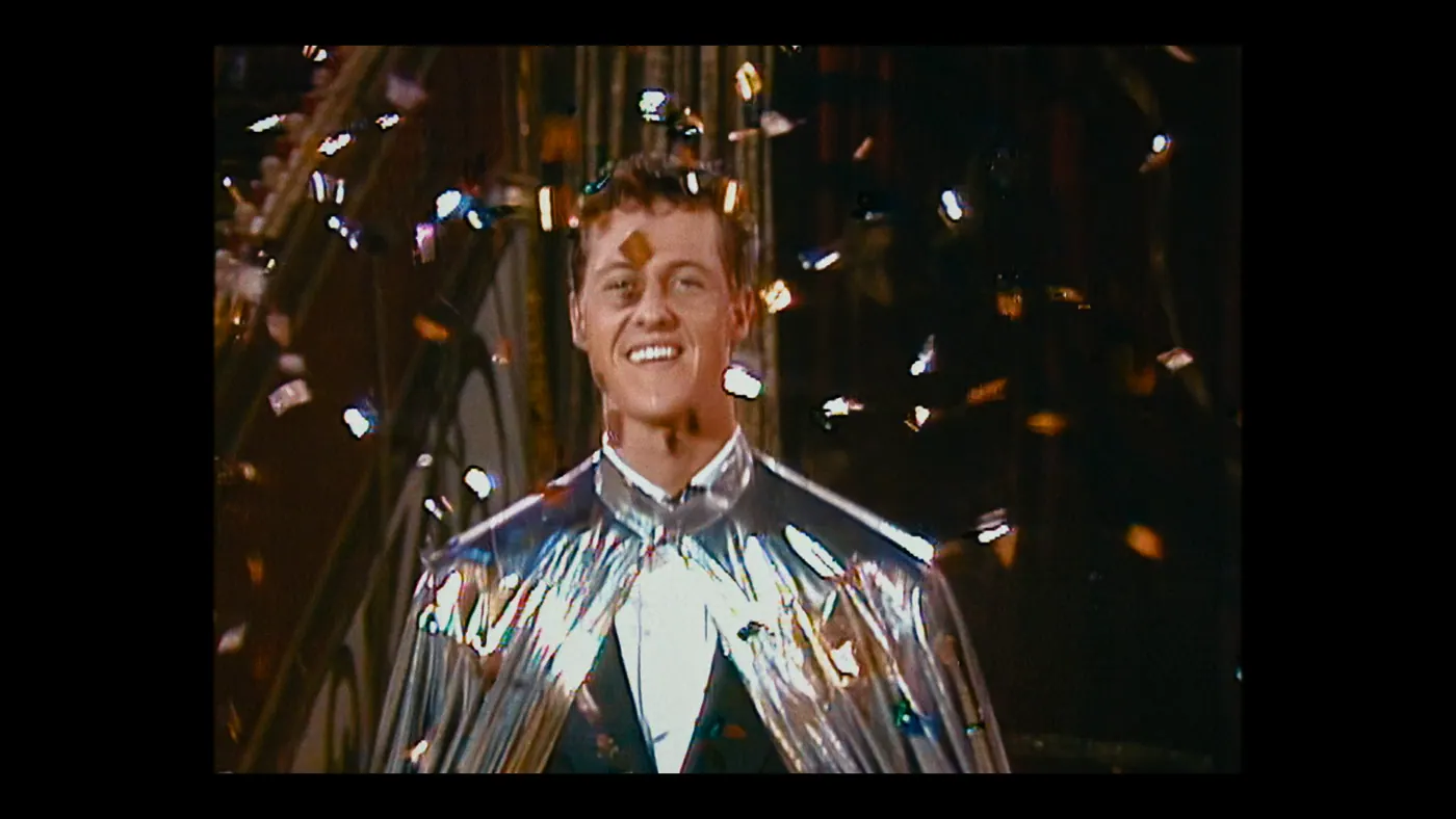 Schumacher ’94 — The Birth of a Legend (2026), Christin Freitag — plan rapproché, intérieur, un personnage, lumière chaude : cape argentée, confetti, rire