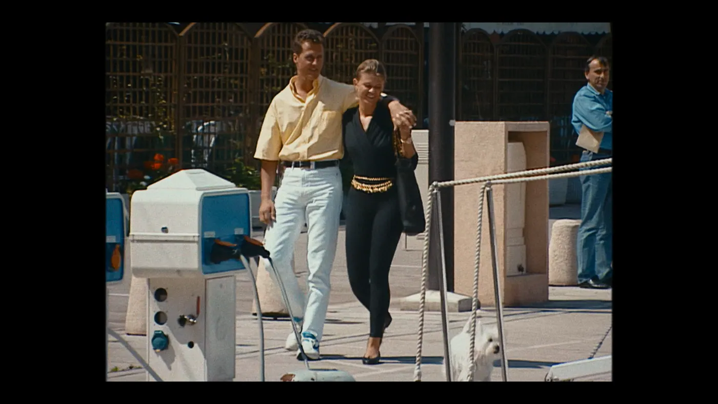 Schumacher ’94 — The Birth of a Legend (2026), Christin Freitag — plan moyen, jour, extérieur, trois personnages, soleil direct : port, chemise jaune, jean blanc, chien, sac à main, corde