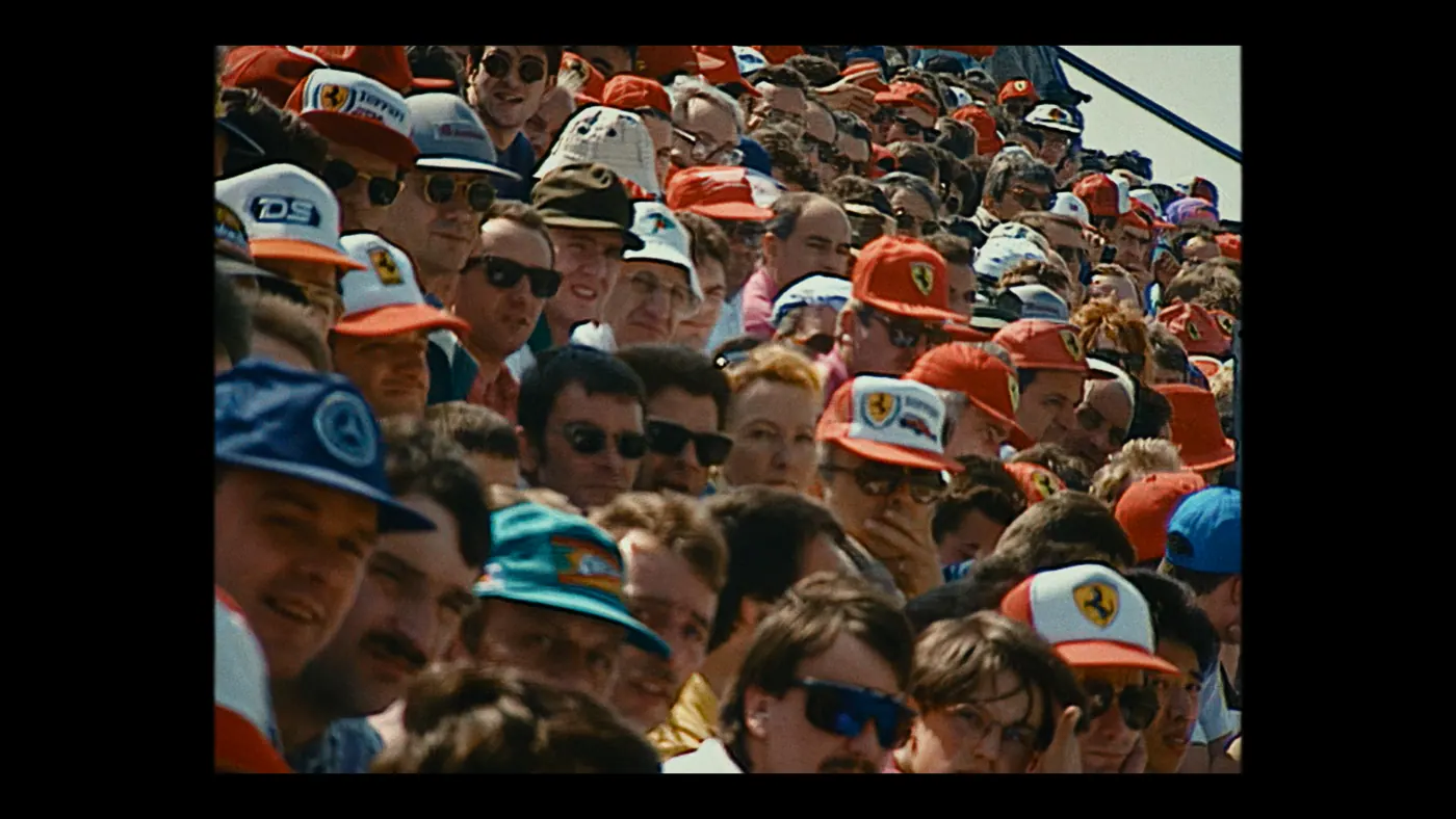 Schumacher ’94 — The Birth of a Legend (2026), Christin Freitag — plan d’ensemble, jour, extérieur, foule, soleil direct : tribune, casquette rouge, lunettes de soleil