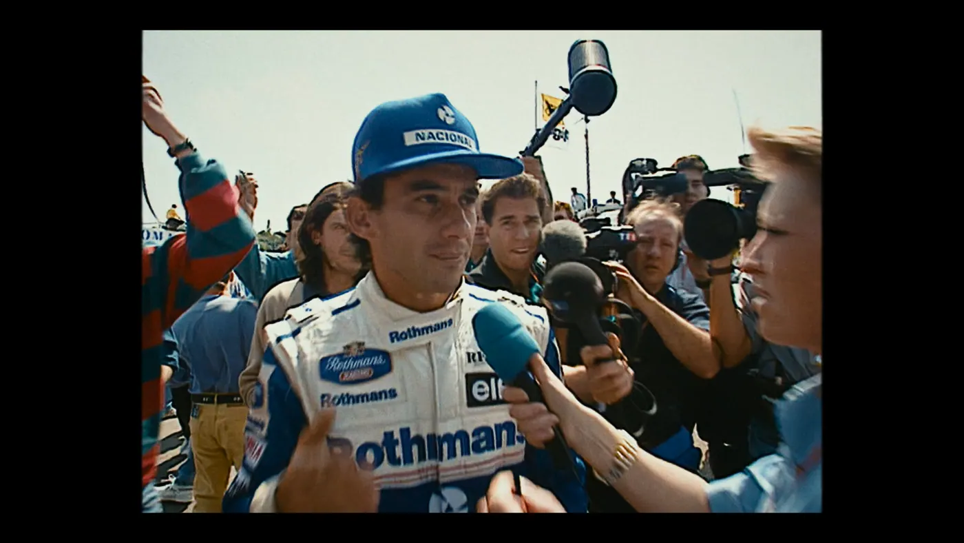 Schumacher ’94 — The Birth of a Legend (2026), Christin Freitag — plan rapproché, jour, extérieur, foule : circuit automobile, casquette bleue, combinaison blanche, micro, caméra, perche