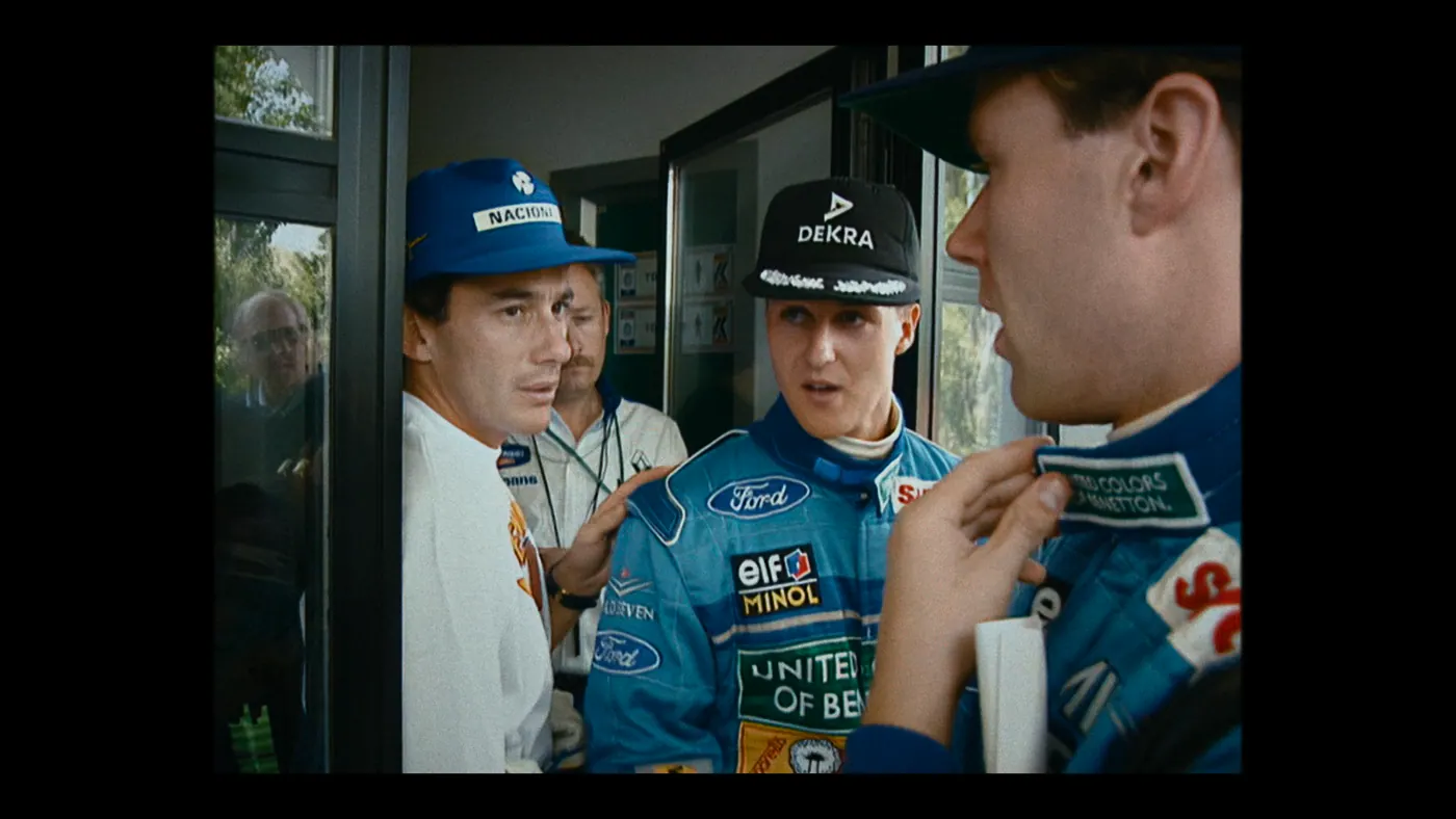 Schumacher ’94 — The Birth of a Legend (2026), Christin Freitag — plan rapproché, jour, cinq personnages : casquette bleue, casquette noire, porte vitrée, combinaison de pilote, tee-shirt