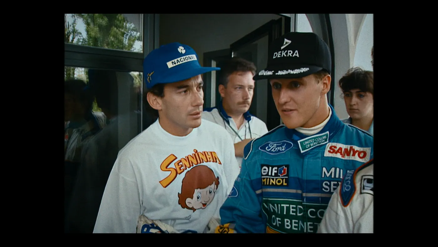 Schumacher ’94 — The Birth of a Legend (2026), Christin Freitag — plan rapproché, jour, cinq personnages : casquette bleue, casquette noire, porte vitrée, combinaison de pilote