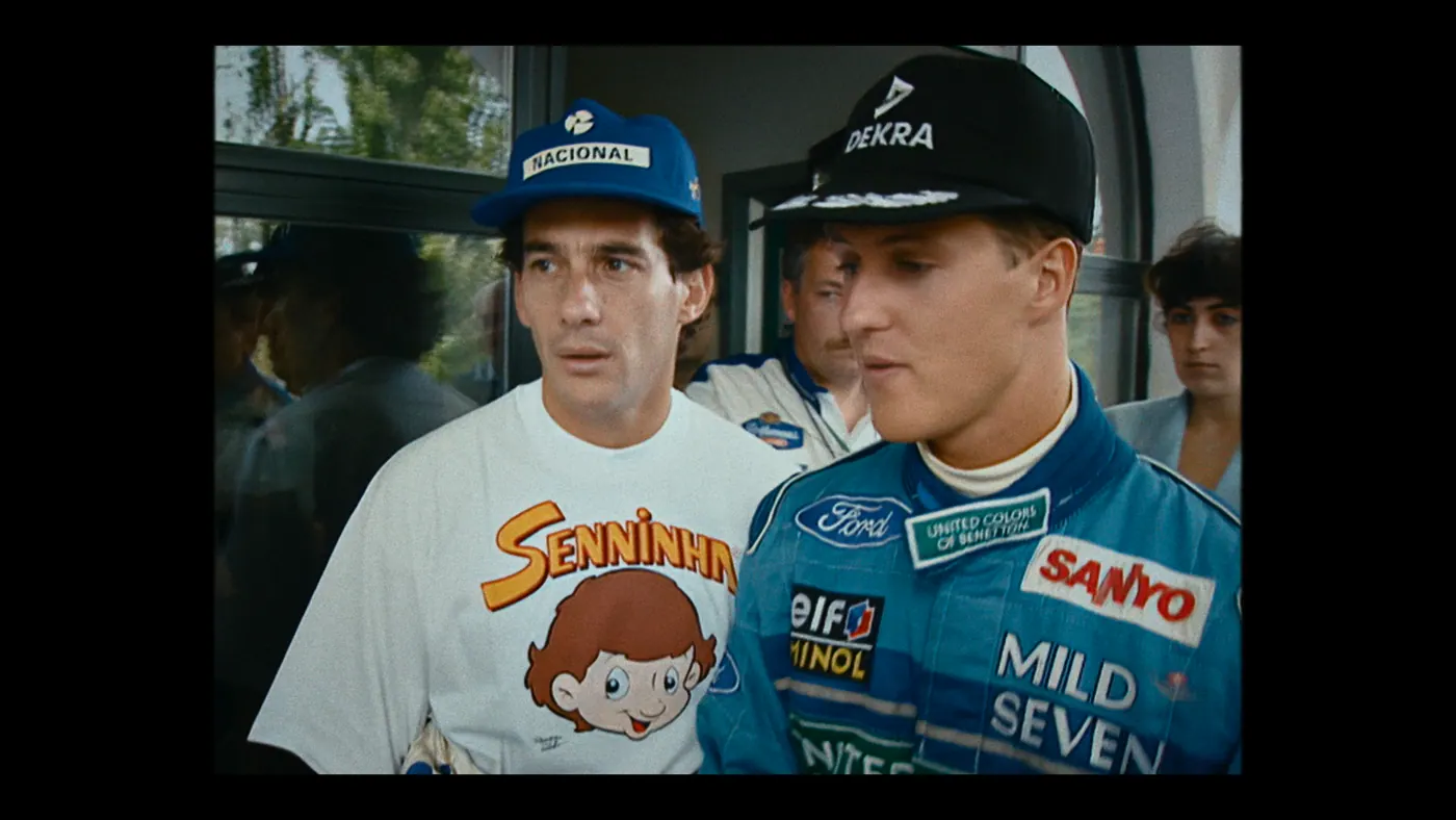 Schumacher ’94 — The Birth of a Legend (2026), Christin Freitag — plan rapproché, jour, cinq personnages : casquette bleue, casquette noire, porte vitrée, combinaison de pilote