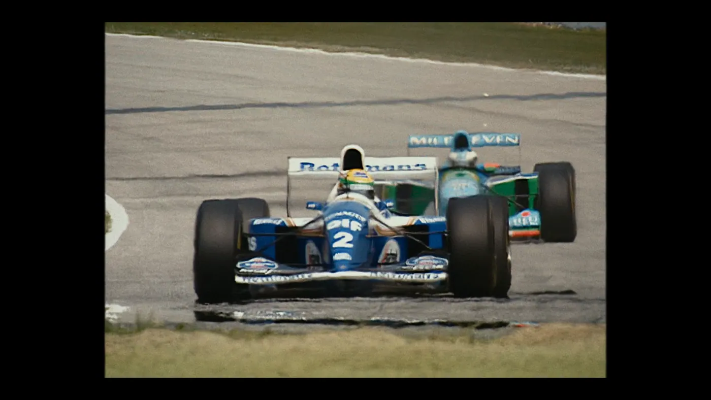 Schumacher ’94 — The Birth of a Legend (2026), Christin Freitag — plan large, jour, extérieur, deux personnages, soleil direct : circuit automobile, voiture de course, formule 1, casque