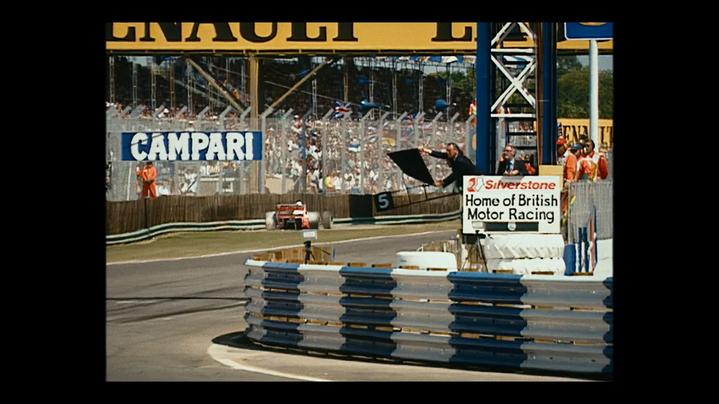 Schumacher ’94 — The Birth of a Legend (2026), Christin Freitag — plan large, jour, extérieur, foule, soleil direct : circuit automobile, combinaison orange, voiture de course, formule 1