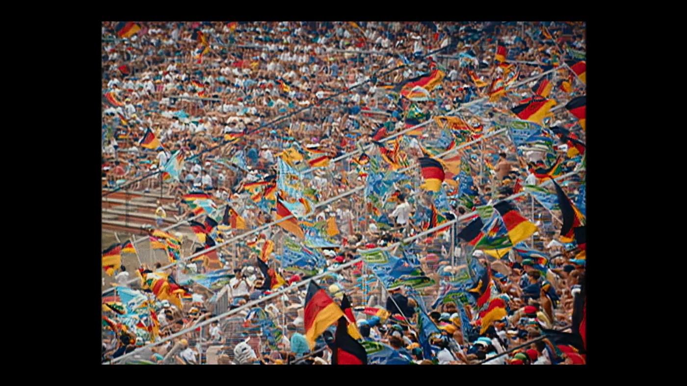 Schumacher ’94 — The Birth of a Legend (2026), Christin Freitag — plan d’ensemble, jour, extérieur, foule : stade, drapeau allemand, drapeau, tribune, casquette, agiter un drapeau