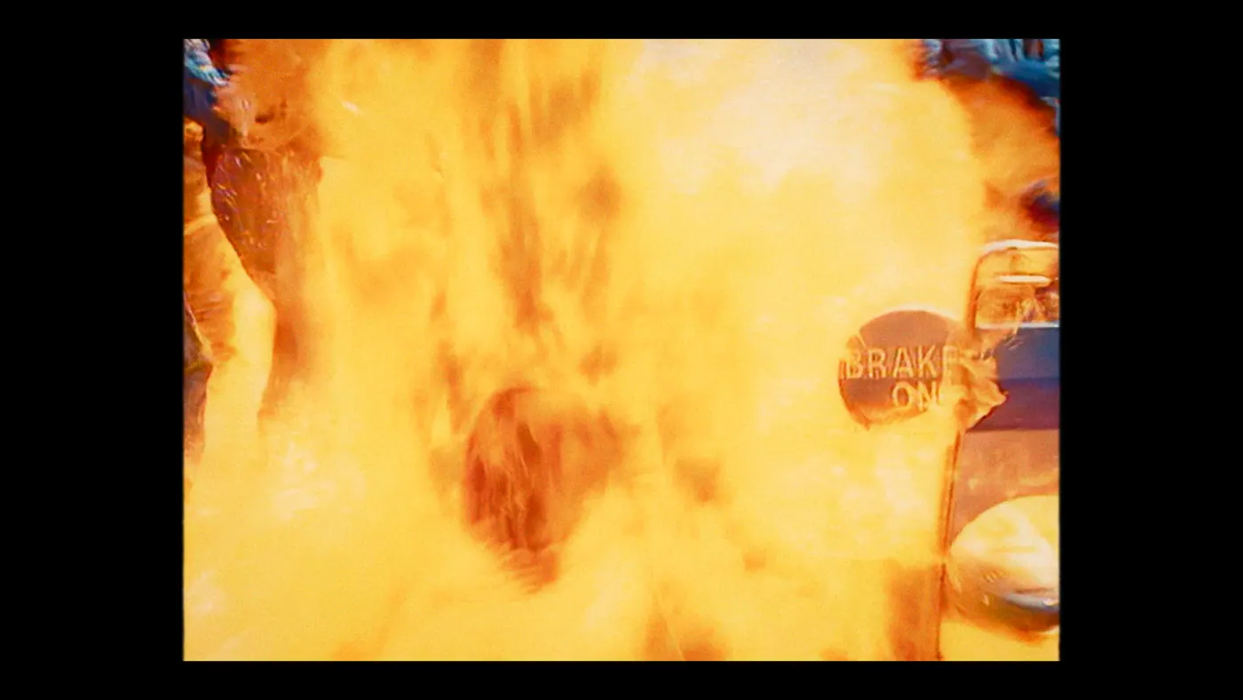 Schumacher ’94 — The Birth of a Legend (2026), Christin Freitag — plan moyen, jour, extérieur, deux personnages, feu : circuit automobile, boule de feu, flamme, panneau, voiture de course