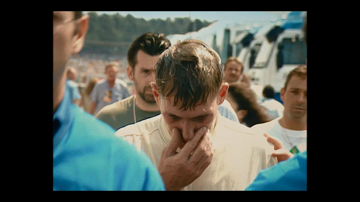 Schumacher ’94 — The Birth of a Legend (2026), Christin Freitag — plan rapproché, jour, extérieur, foule, soleil direct : circuit automobile, col roulé blanc, camion, tribune, tee-shirt