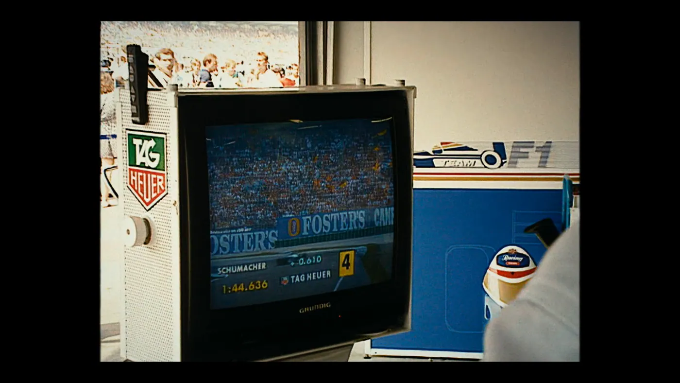 Schumacher ’94 — The Birth of a Legend (2026), Christin Freitag — insert, jour, foule : circuit automobile, téléviseur, logo, formule 1, casque