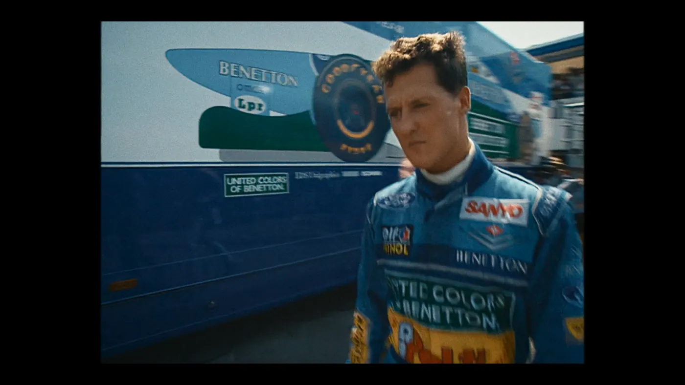 Schumacher ’94 — The Birth of a Legend (2026), Christin Freitag — plan rapproché, jour, extérieur, un personnage, soleil direct : circuit automobile, combinaison bleue, camion, pneu