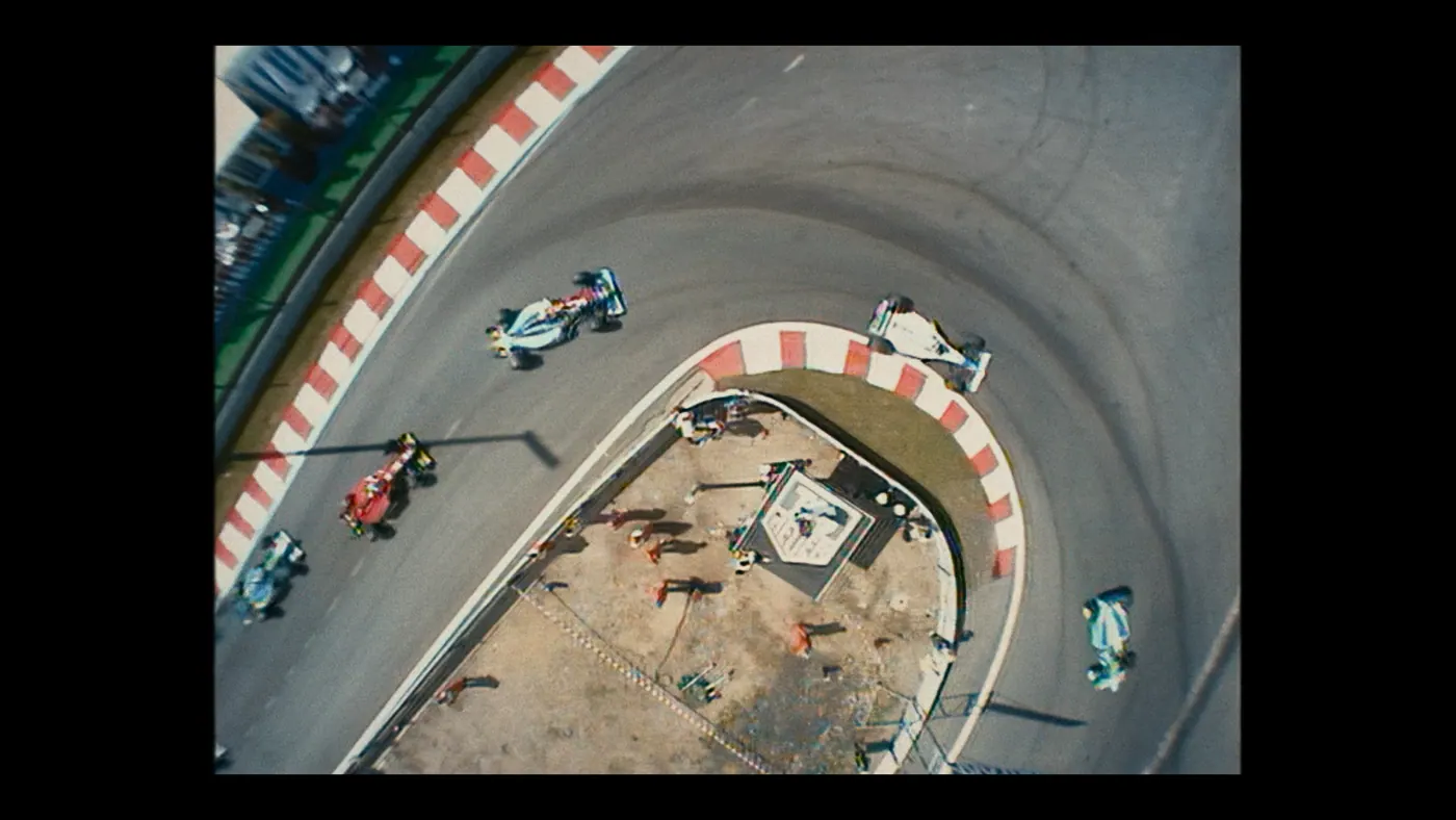 Schumacher ’94 — The Birth of a Legend (2026), Christin Freitag — plan d’ensemble, jour, extérieur, foule, soleil direct : circuit automobile, combinaison orange, voiture de course
