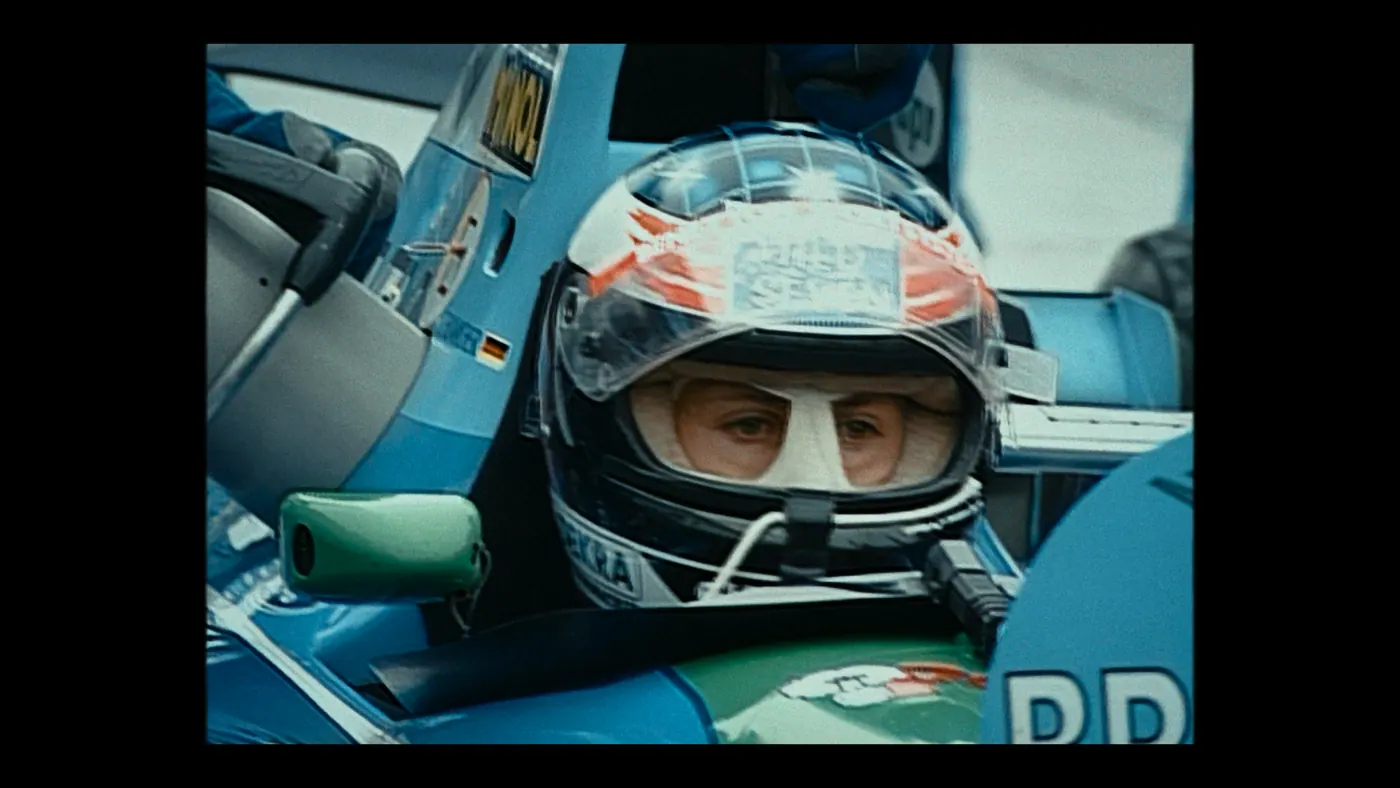Schumacher ’94 — The Birth of a Legend (2026), Christin Freitag — plan rapproché, jour, deux personnages : voiture (habitacle), cagoule blanche, voiture de course, formule 1, rétroviseur