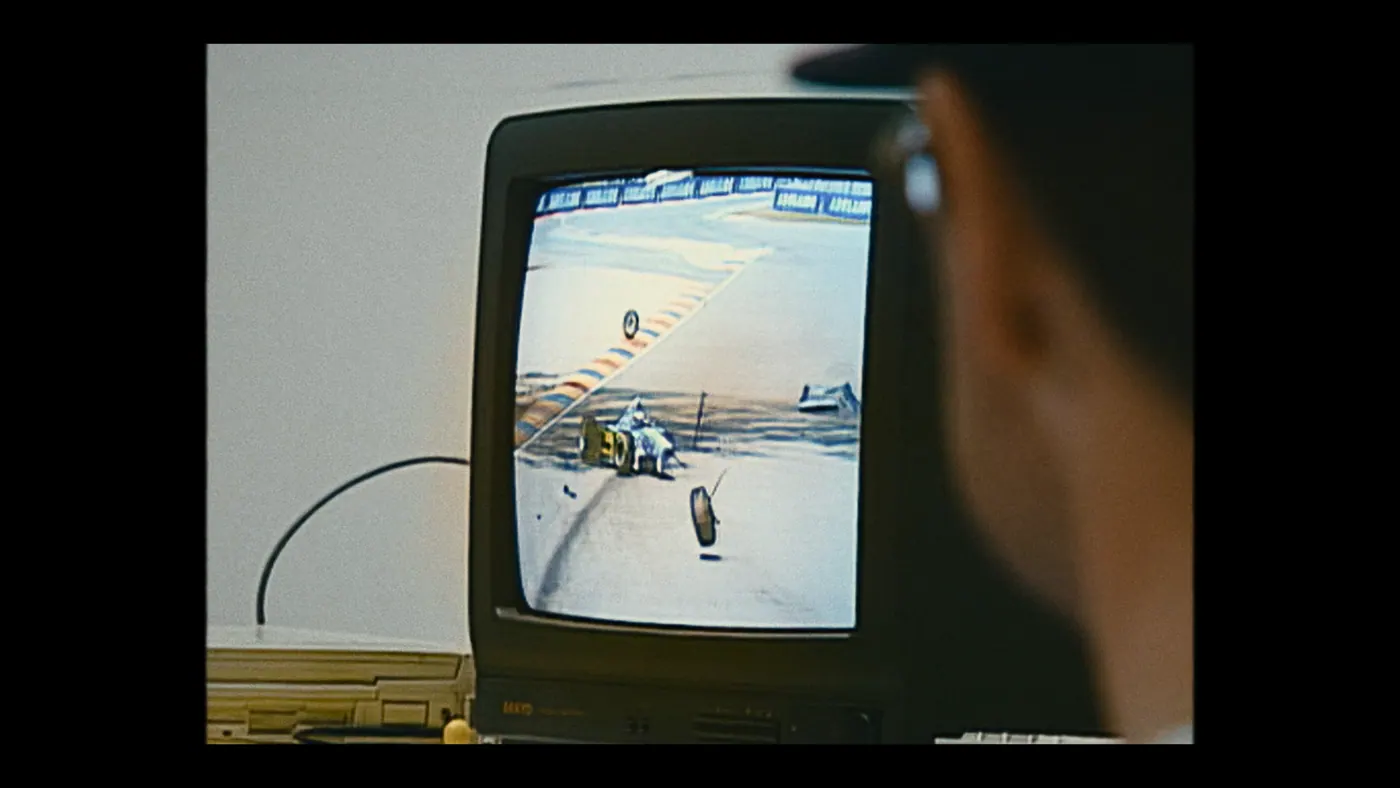 Schumacher ’94 — The Birth of a Legend (2026), Christin Freitag — plan rapproché, intérieur, un personnage : téléviseur, ordinateur, câble, voiture de course, formule 1, casquette, lunettes