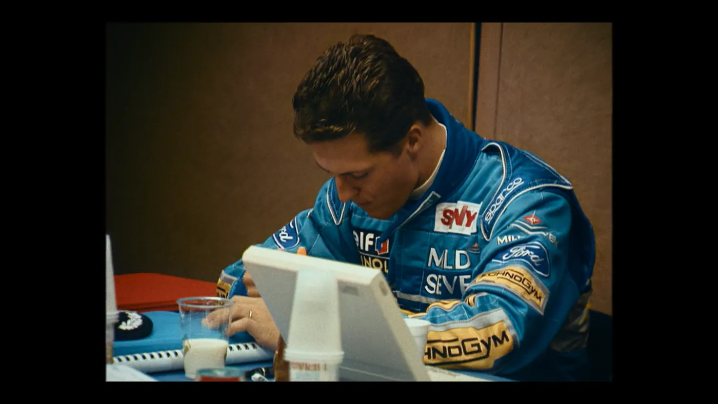 Schumacher ’94 — The Birth of a Legend (2026), Christin Freitag — plan rapproché, intérieur, un personnage : bureau, combinaison bleue, verre de lait, gobelet, cahier, bague