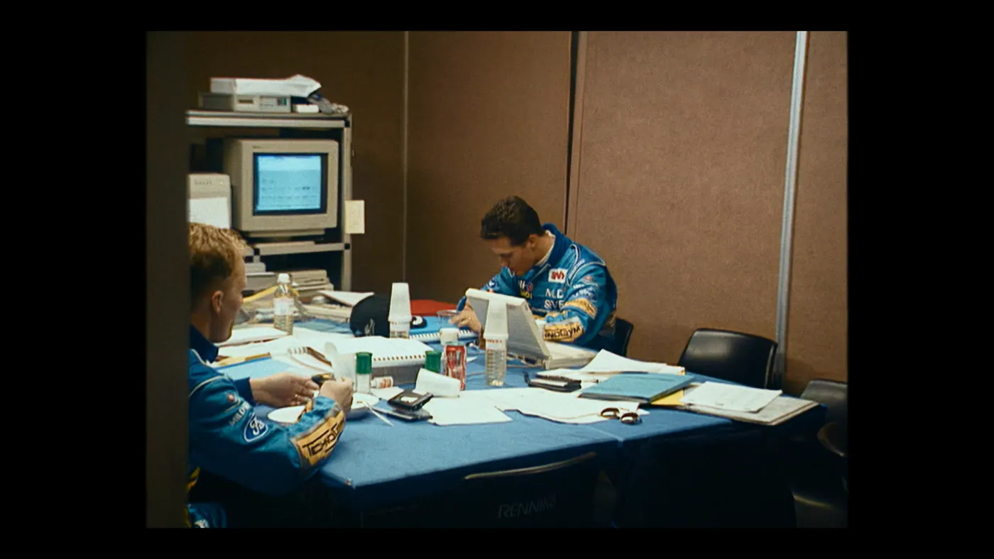 Schumacher ’94 — The Birth of a Legend (2026), Christin Freitag — plan large, intérieur, deux personnages : bureau, combinaison bleue, ordinateur, écran d’ordinateur, gobelet