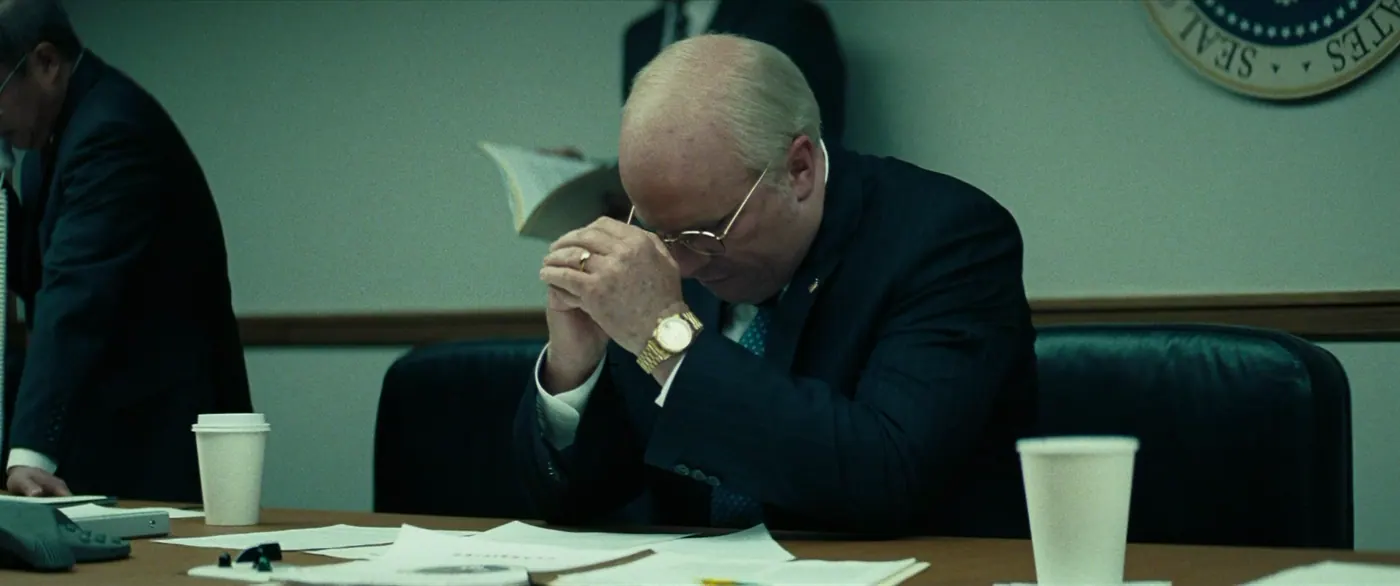 Vice (2018), Adam McKay — plan rapproché, intérieur, trois personnages, lumière froide : bureau, montre, bague, lunettes, gobelet, téléphone fixe, costume, cravate