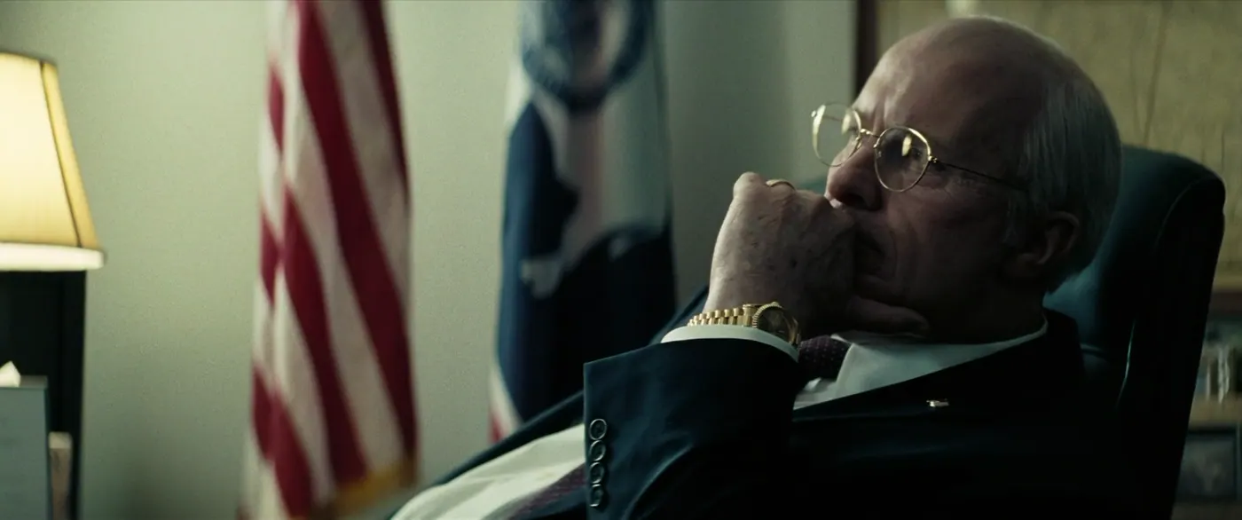 Vice (2018), Adam McKay — plan rapproché, intérieur, un personnage, lumière froide, lumière chaude : bureau, drapeau américain, drapeau, lampe, montre, bague, costume, cravate