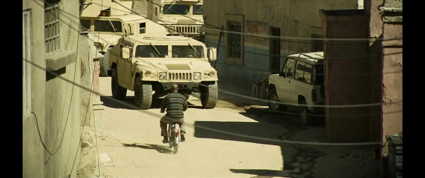 Vice (2018), Adam McKay — plan large, jour, extérieur, un personnage, soleil direct : rue, ville, humvee, véhicule militaire, deux-roues, 4x4, fil électrique, pull rayé