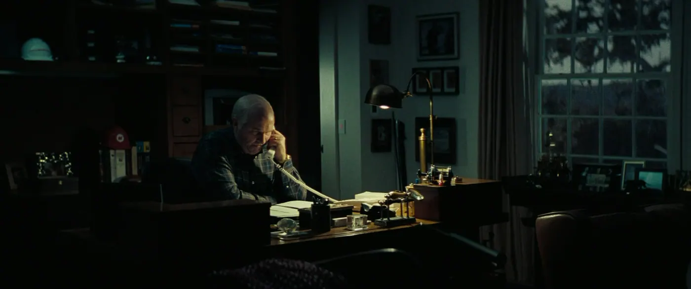 Vice (2018), Adam McKay — plan large, nuit, intérieur, un personnage, clair-obscur, lumière froide : bureau, téléphone fixe, lampe de bureau, bibliothèque, livre, casque de chantier
